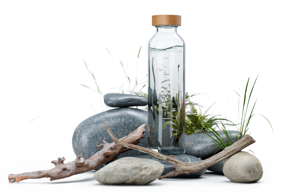 Botella de vidrio Flaska con agua, en una composición con piedras, madera y plantas que evoca naturaleza y bienestar.