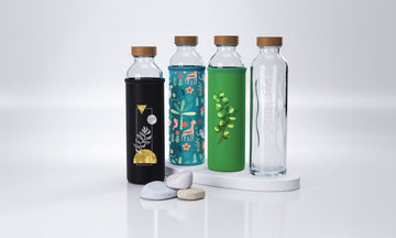 Cuatro botellas de cristal Flaska con tapón de madera, que llevan fundas de neopreno con diversos diseños coloridos.