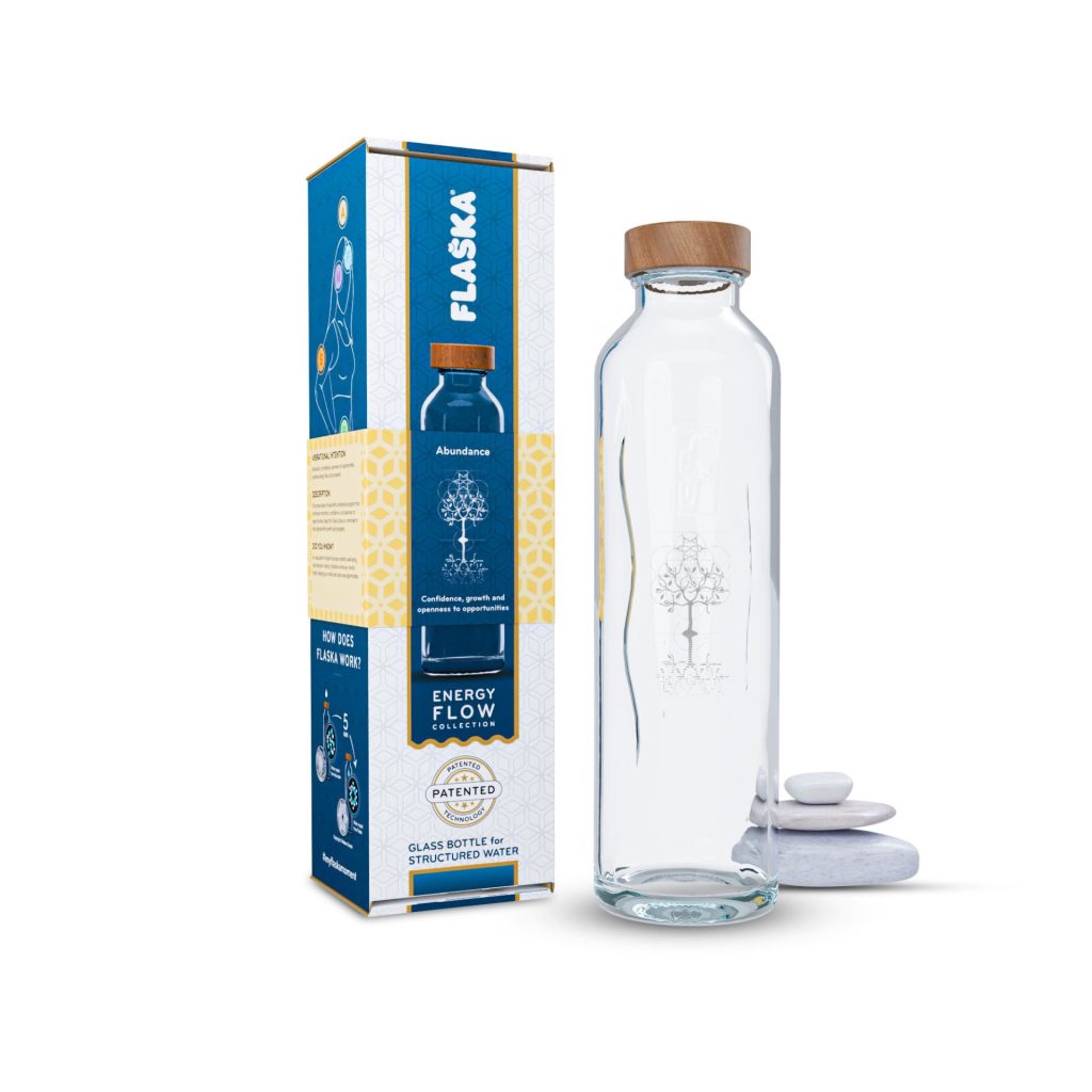 La botella de agua Flaska Abundance para el crecimiento personal, junto a su caja y unas piedras apiladas.