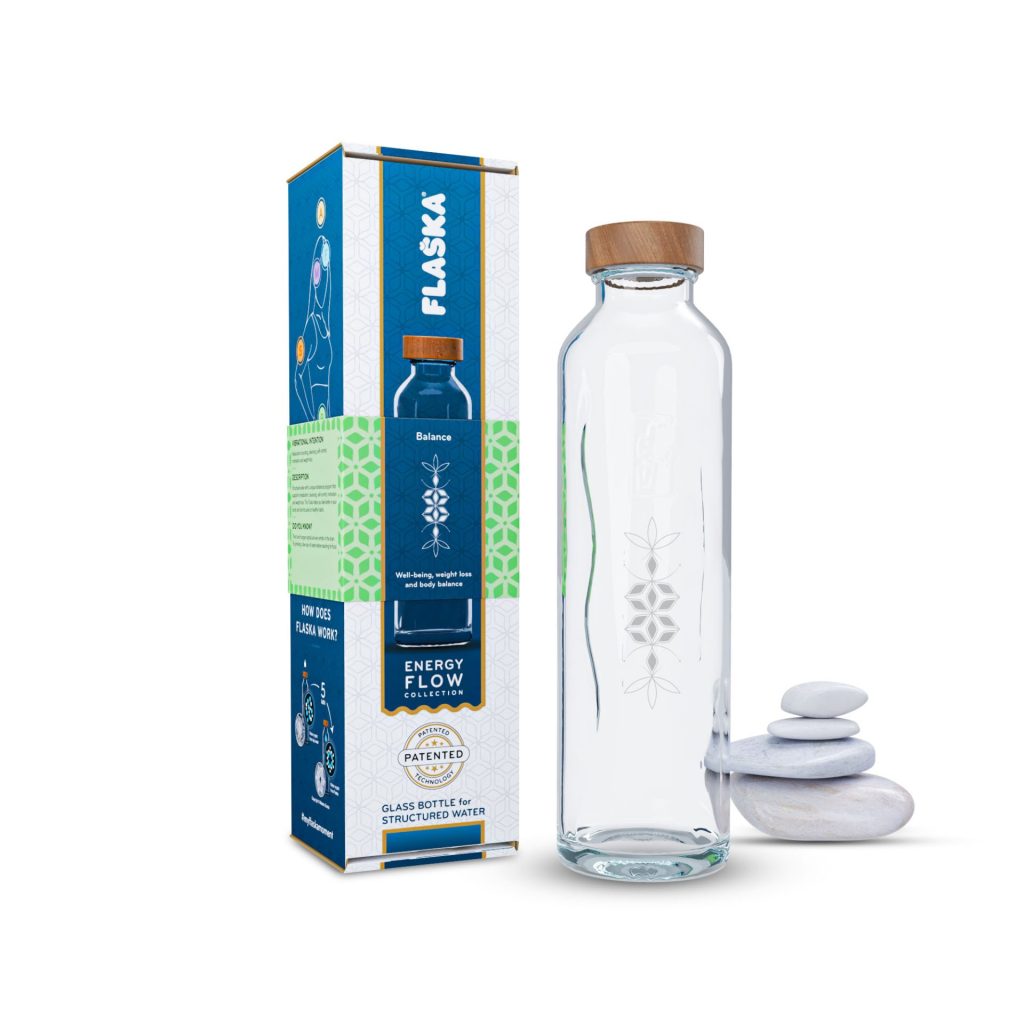 La botella de cristal programado Flaska Balance, de la colección Energy Flow, exhibida junto a su empaque y piedras.
