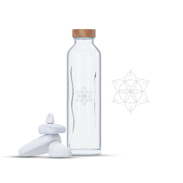 Botella de cristal programado con tapón de madera junto a piedras blancas en equilibrio y diseño geométrico.