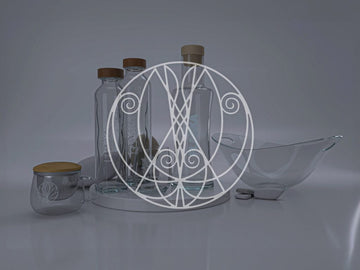 Un juego de botellas de vidrio Flaska, acompañadas de un cuenco y una taza con tapas de madera, expuestas sobre una superficie reflectante con un elaborado patrón del cosmograma de Flaska.